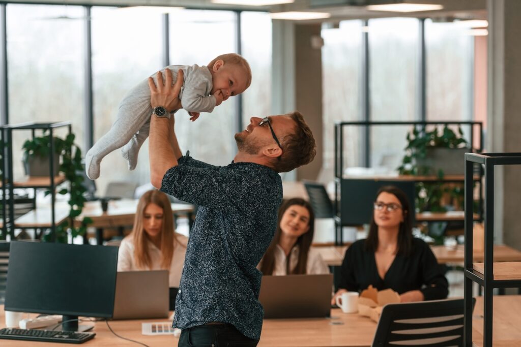 A man in glasses holds a baby in an office that supports mental health support for new dads.