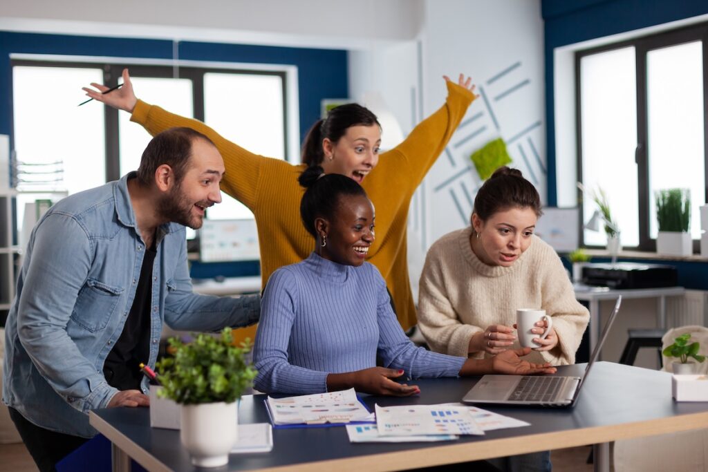 A team celebrates at a desk to represent a positive workplace culture.